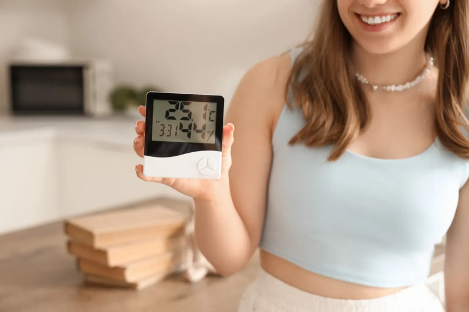 Smilende kvinde holder et digitalt hygrometer frem i et køkken