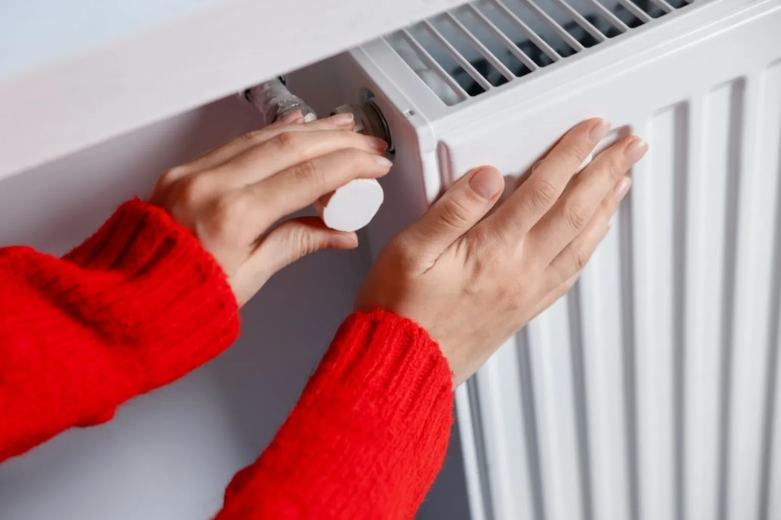Kvinde i rød trøje justerer termostaten og mærker på radiatoren