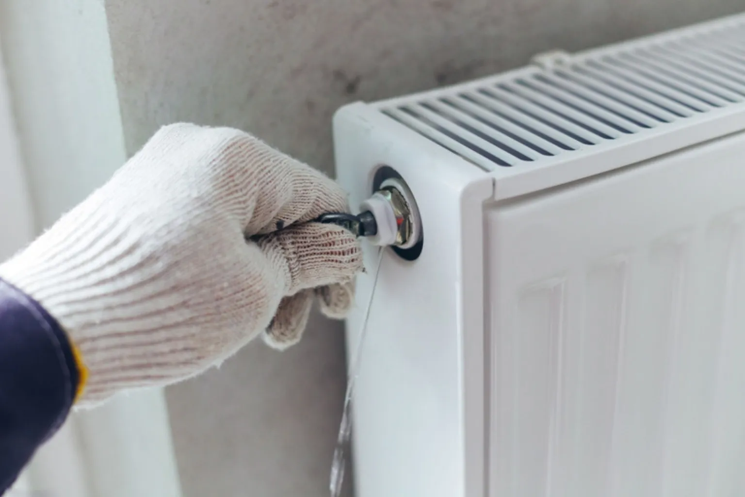 Hånd i arbejdshandske lufter en radiator ud med en radiatornøgle