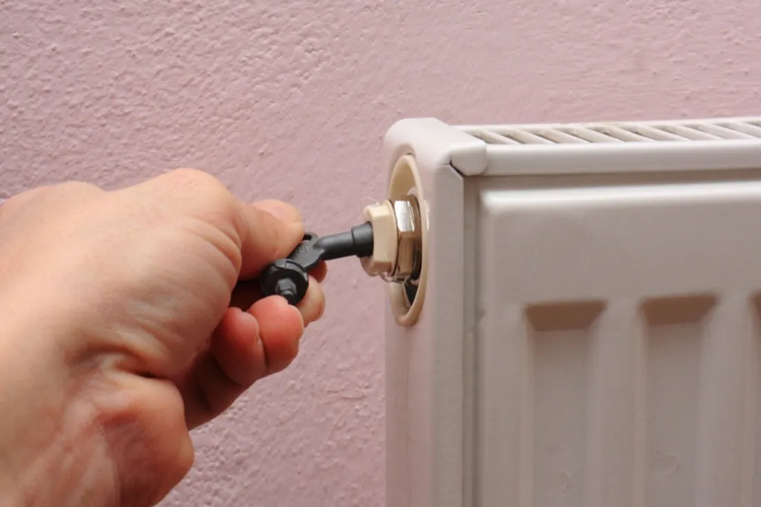 Hånd drejer en radiatornøgle i udluftningsskruen på en hvid radiator