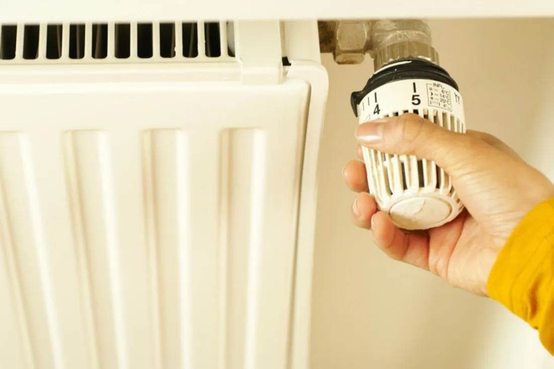 Hånd drejer termostaten på en hvid radiator