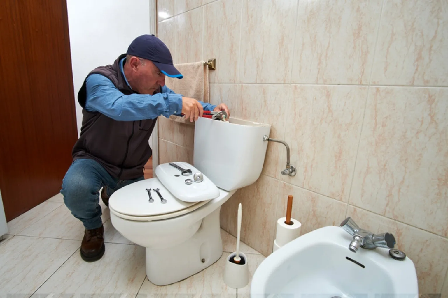 VVS-montør på knæ ved et toilet med låget af cisternen